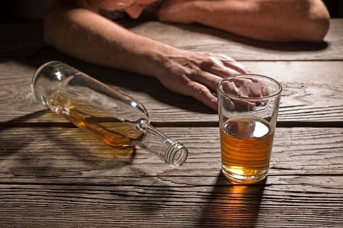 Мужчина лежит на столе рядом с алкоголем